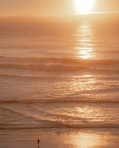 Lone figure walking on a glowing golden beach at sunset