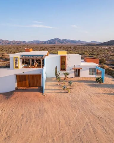 Modern white and orange house with garage on dirt driveway in desert landscape with mountains in distance