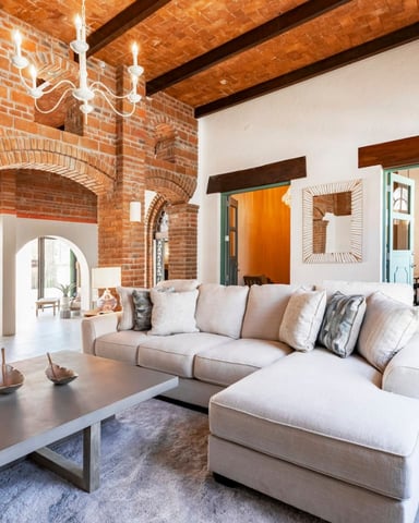 Open-plan loft with exposed brick walls, wooden beams, cream sectional sofa, and metal coffee table