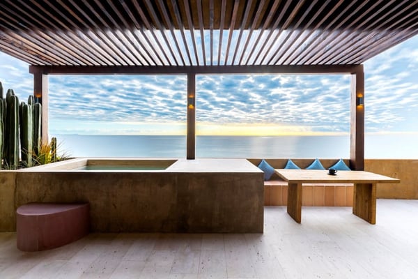 Modern rooftop terrace with slatted pergola, wooden bench, ocean view, and blue cushioned seating