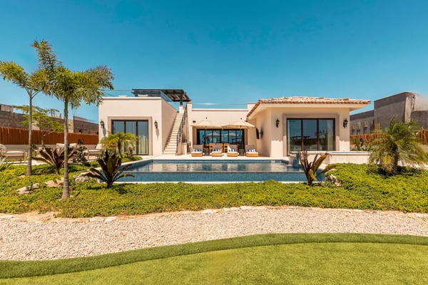 Modern beige villa with swimming pool, palm trees, and manicured lawn under clear blue sky