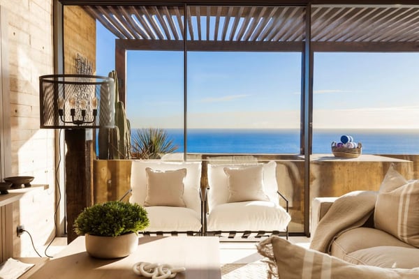 Coastal living room with cream seating, slatted pergola, and expansive ocean view through floor-to-ceiling windows
