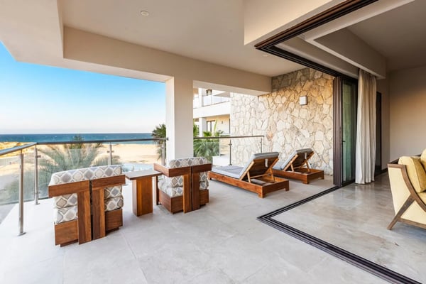 Beachfront terrace with wooden lounge chairs, stone accent wall, and ocean view