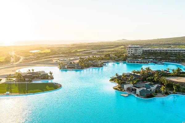 Aerial view of geothermal resort with turquoise lagoon, hotel buildings, and palm trees surrounded by Icelandic lava fields at sunset