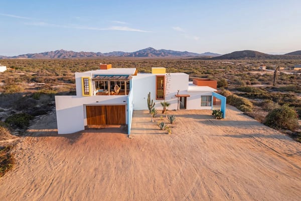 Modern white house with colorful trim on desert landscape with mountains in background